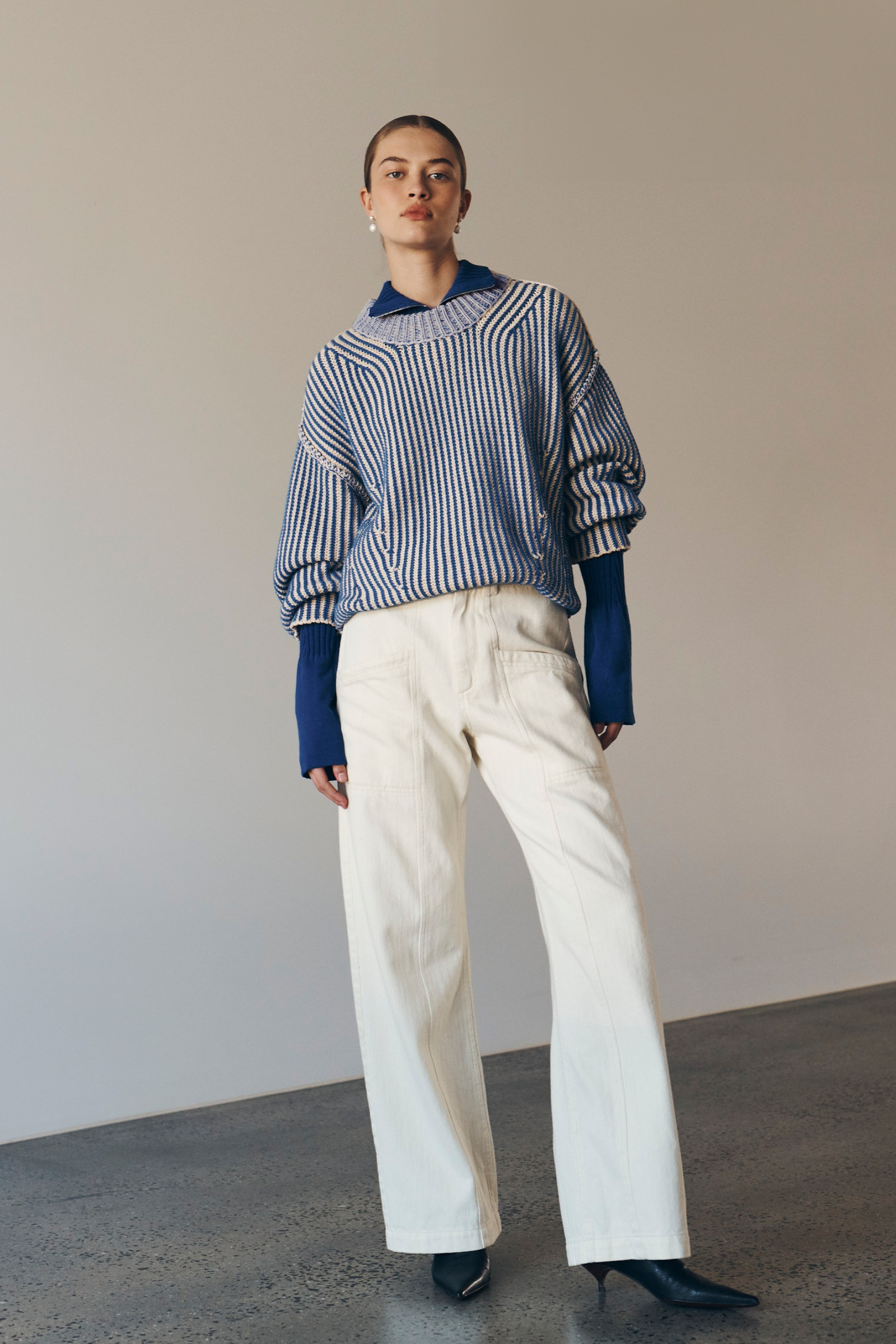 Bianca wears the Tish Knit Jumper in Cobalt over the Travis Zip Knit Top in Cobalt paired with the Gio Jeans in Cream. She accessorises with pearl drop earrings and completes the look with a low, slick bun. 